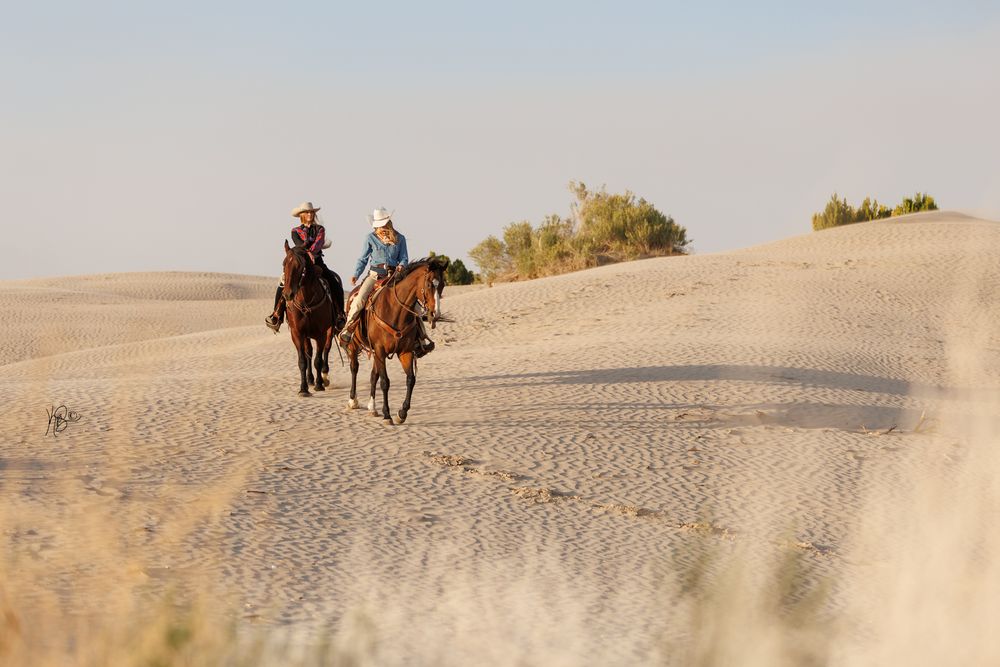 Two cowgirls riding in the sand dunes.