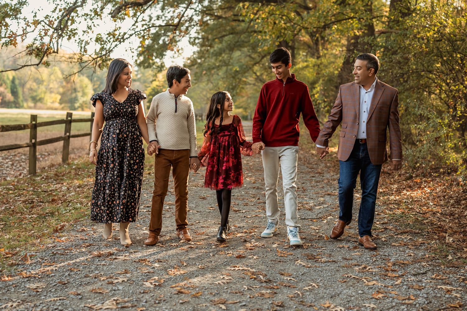 A family walks together on a leaf-covered autumn path through the woods during a fall photoshoot.