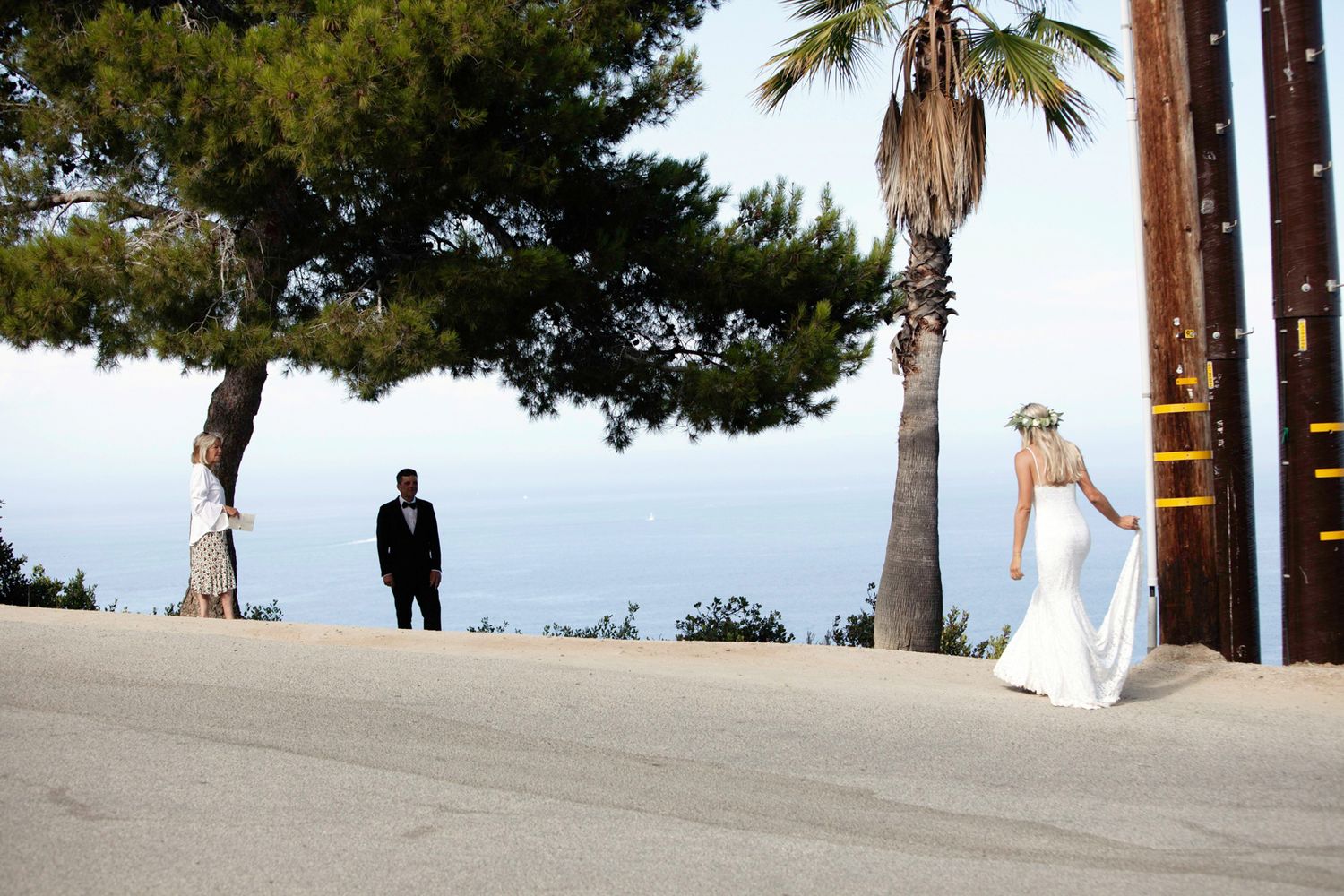 A couple poses for wedding photos under palm trees along a row of columns at oceanfront resort location.