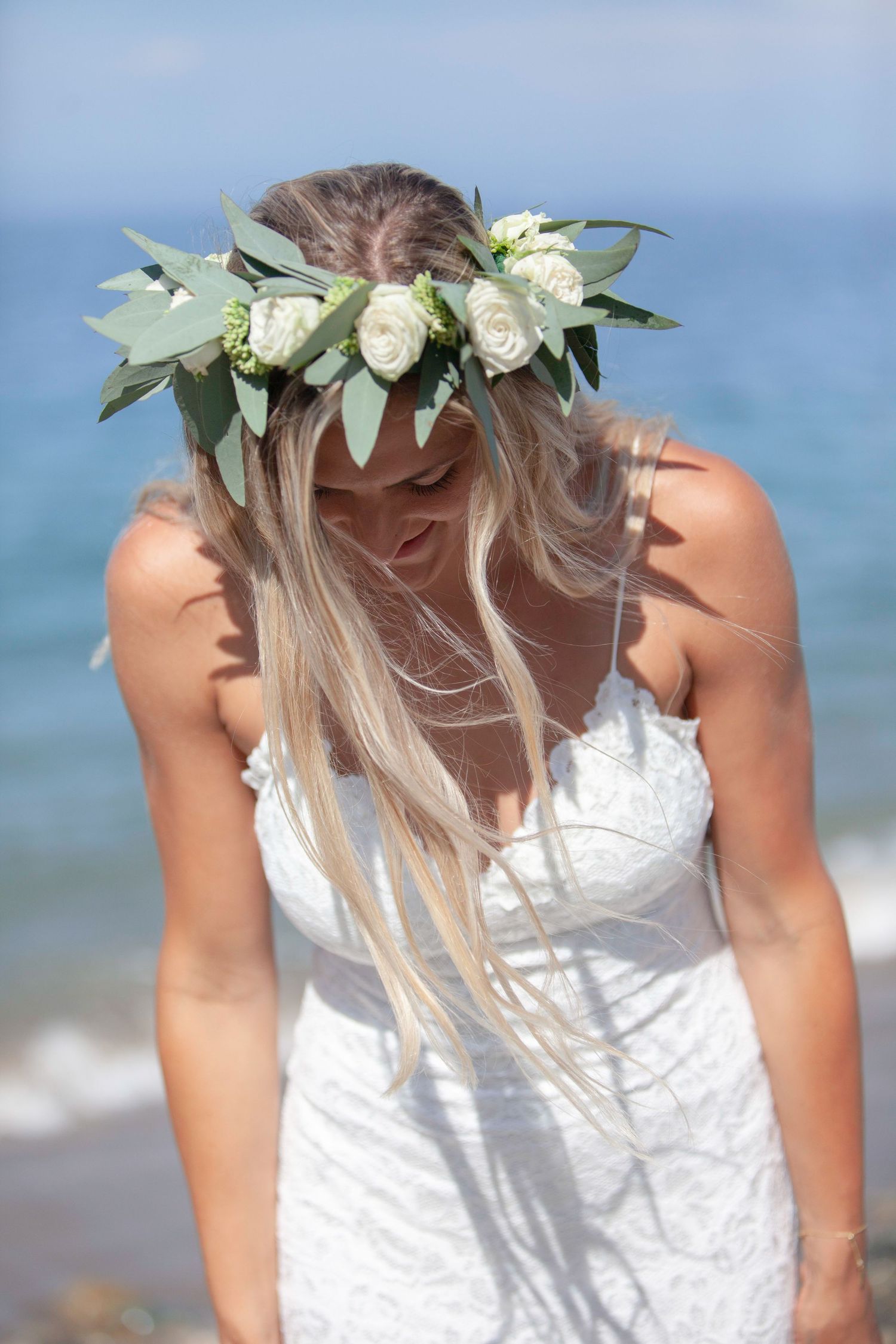 Delicate floral crown adorns a white summer dress against a dreamy ocean backdrop.