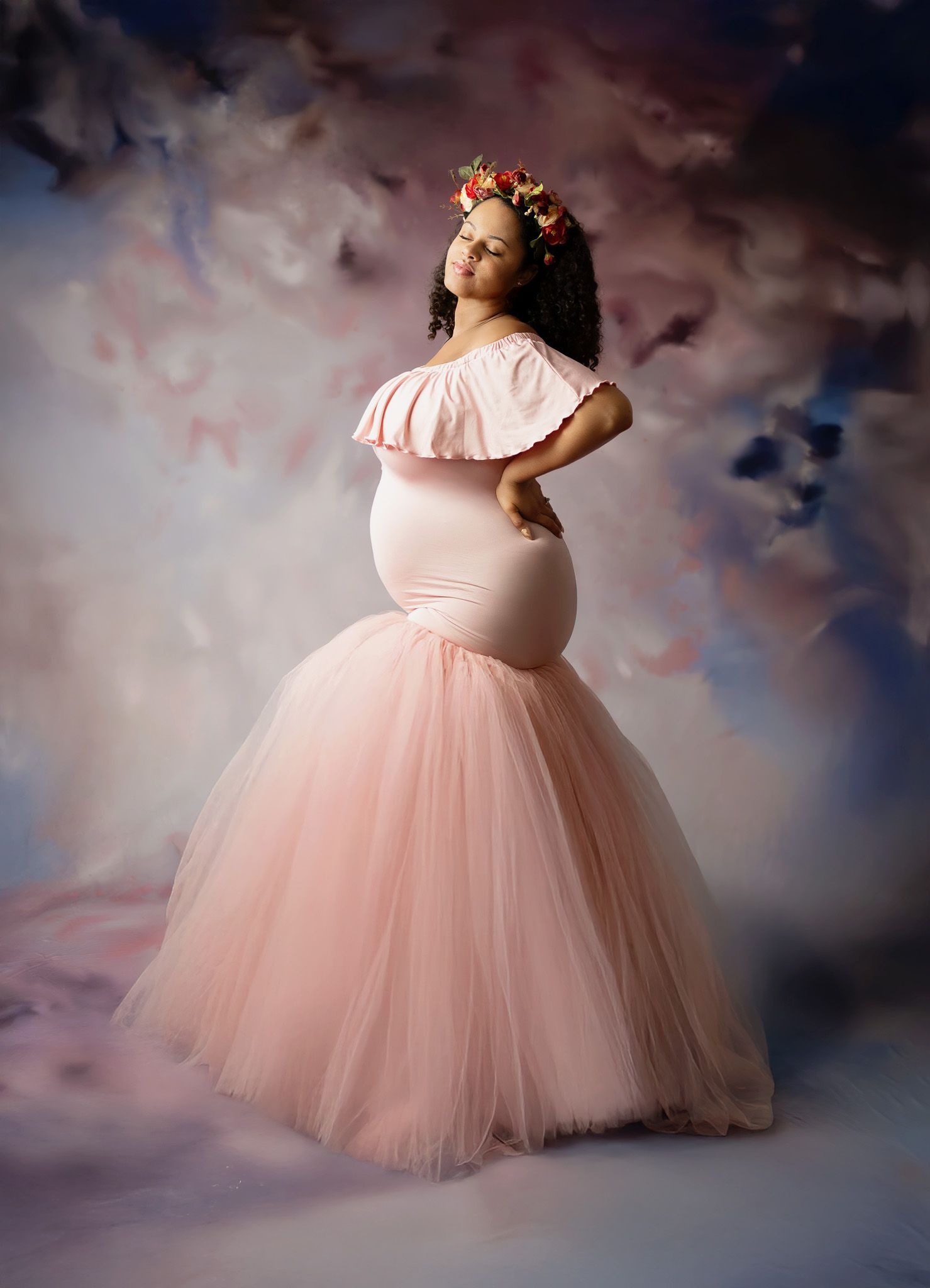 Elegant maternity photoshoot featuring a flowing pink off-shoulder tulle gown against a textured brown backdrop.