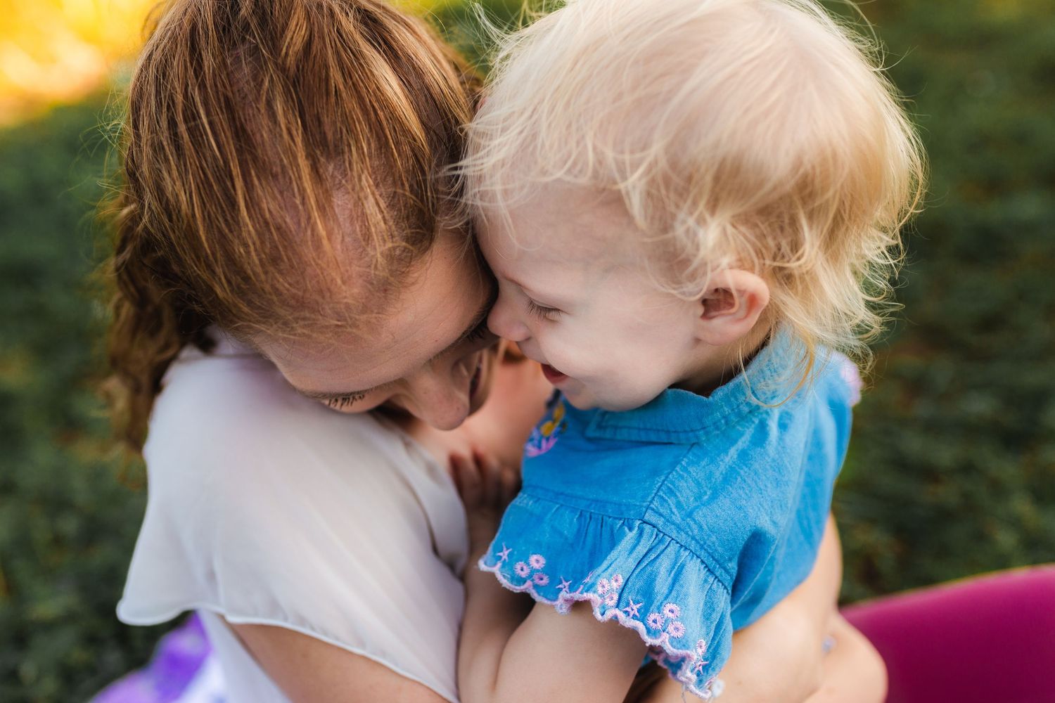 A tender moment of affection shared between parent and child in a sunny outdoor setting.