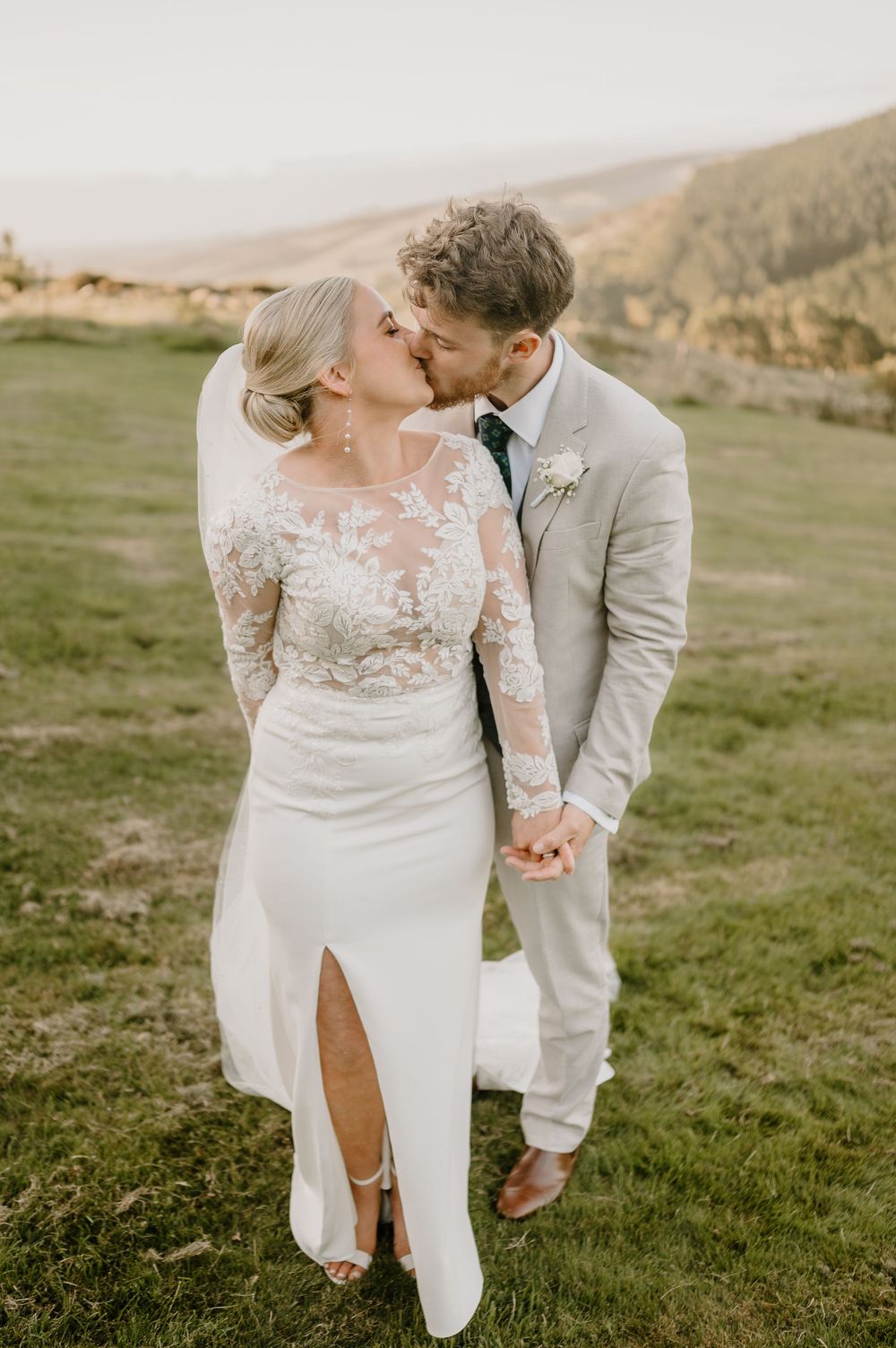 Romantic wedding portrait in a scenic mountainside setting featuring an elegant lace gown and light colored suit.