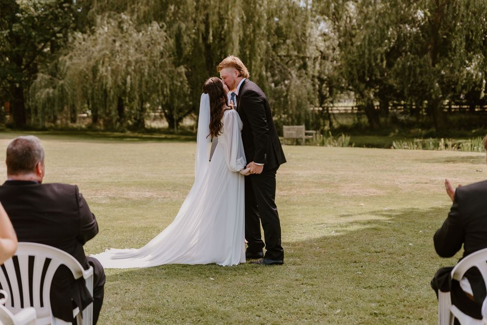 Wedding party stands in a row on grassy lawn during an outdoor ceremony while the officiant speaks.