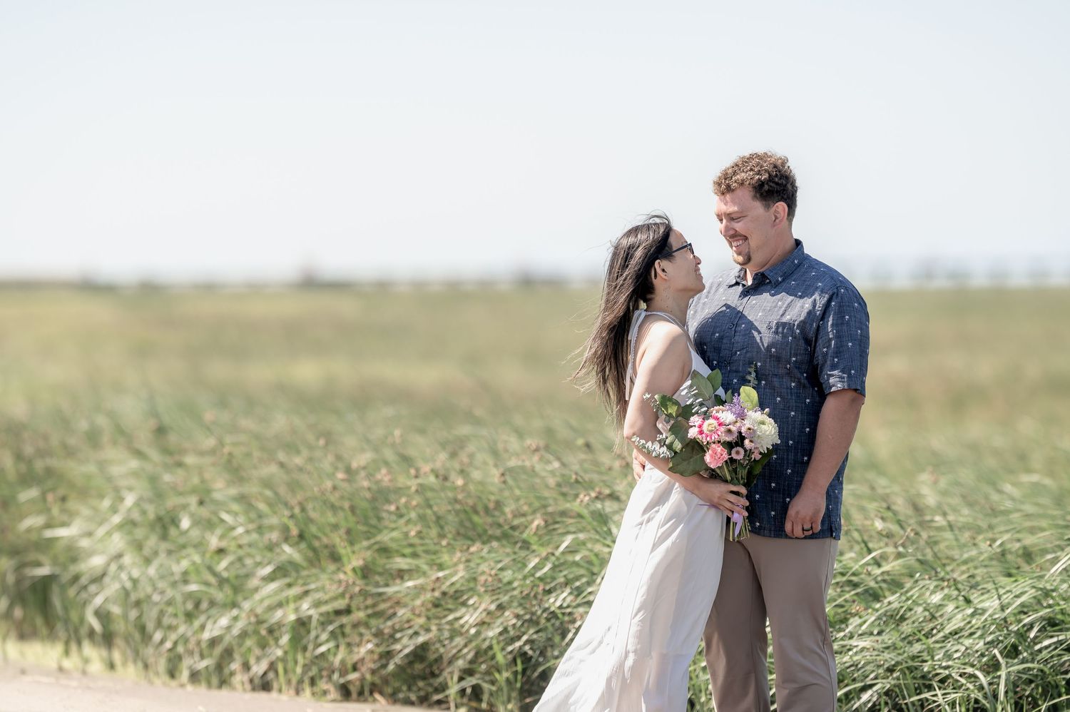 A couple in a scenic grassland field shares a tender romantic moment at sunset during their wedding photoshoot.