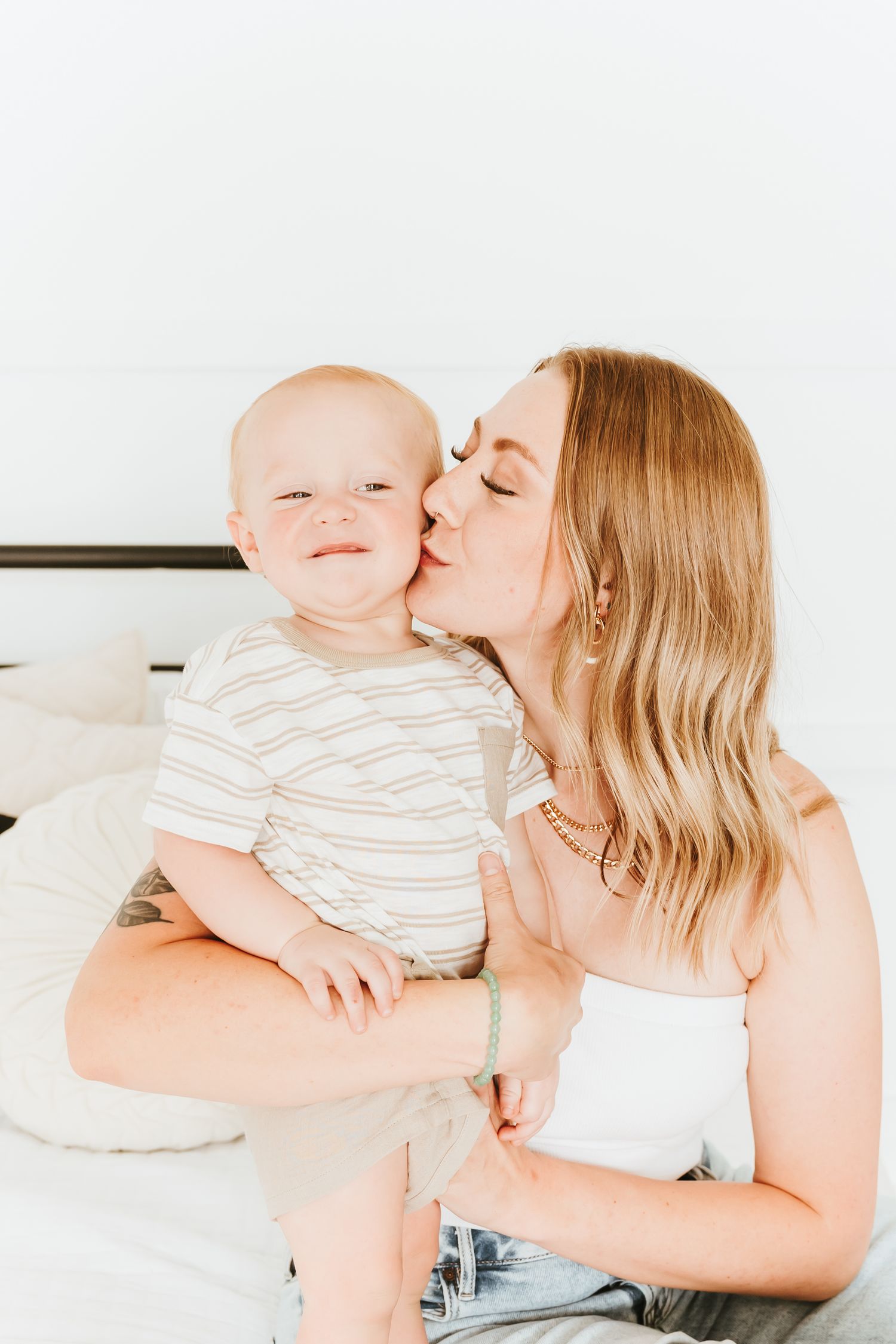 Sweet candid moment between mother and baby laughing and cuddling on white bedding.