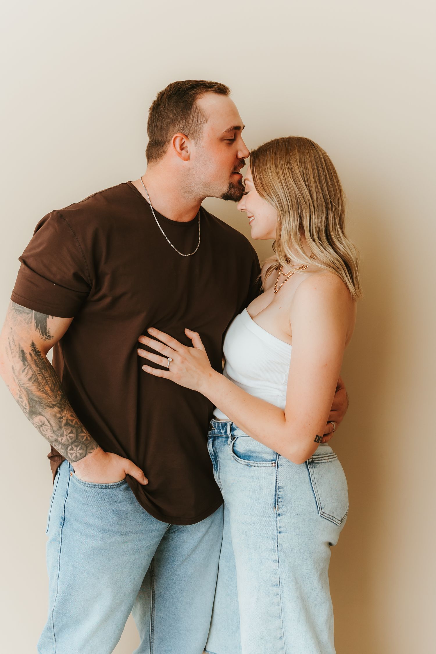 A couple in casual attire share intimate moments against a beige wall in a series of connected photos.