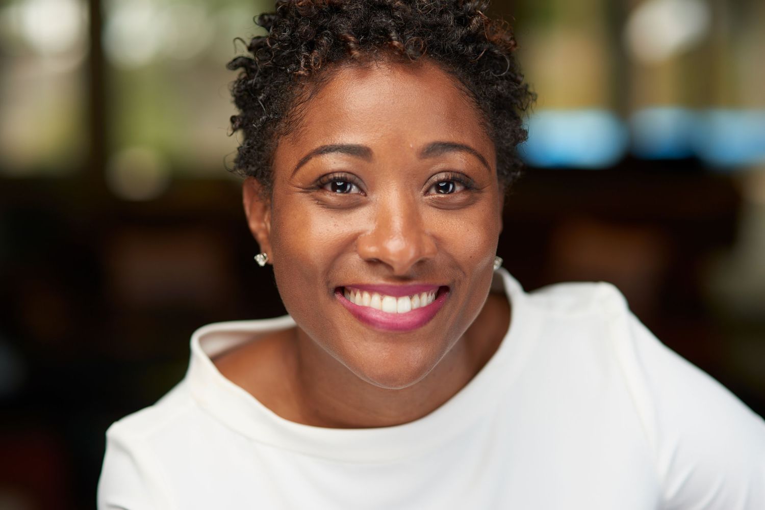 Smiling Black woman in white top with short natural hair in warm bokeh background portrait.