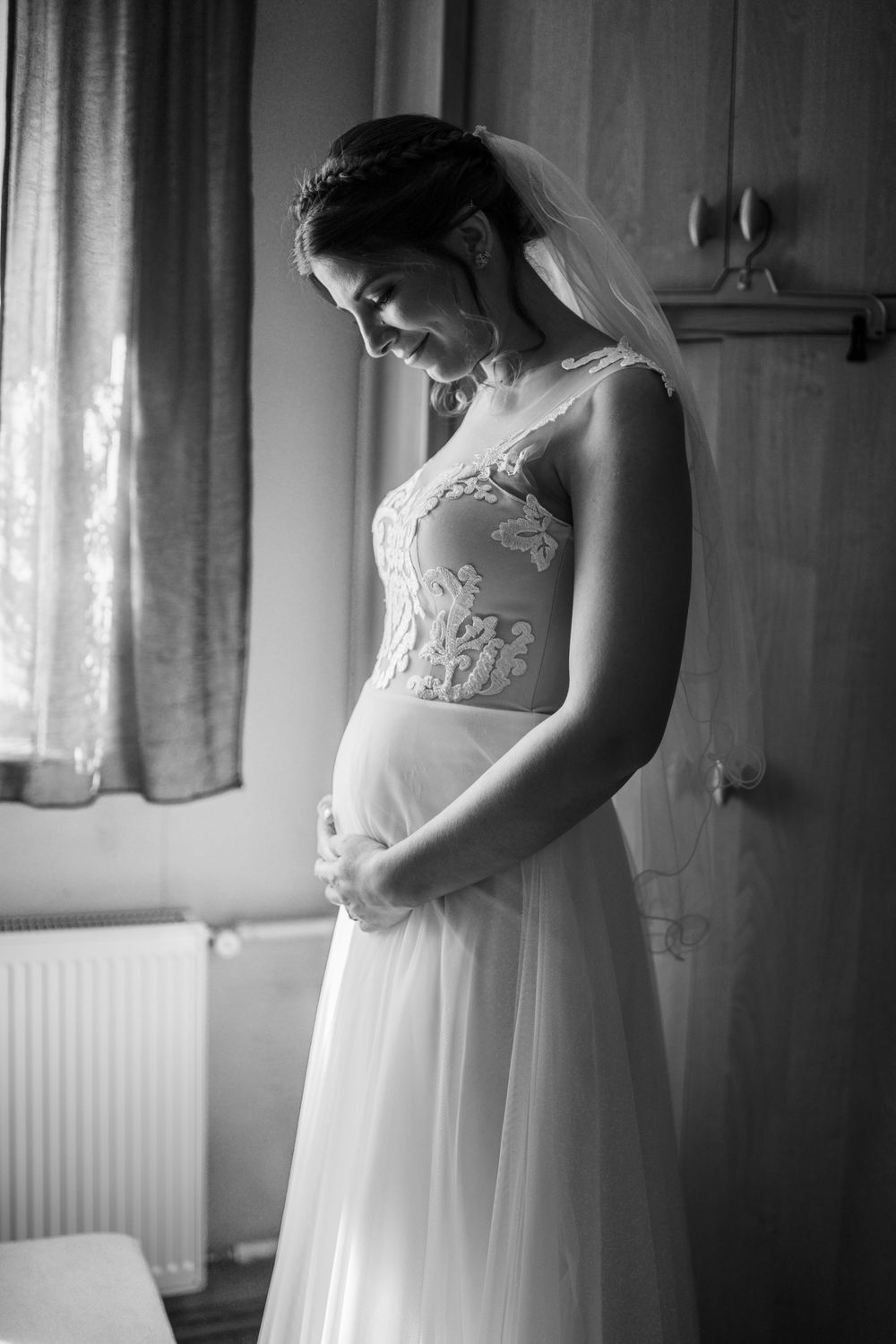 Black and white photos show a bride getting ready in an elegant lace wedding dress by a window.