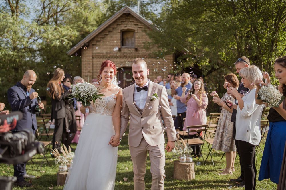 Wedding guests gather outdoors to celebrate on a sunny day near rustic farm buildings.