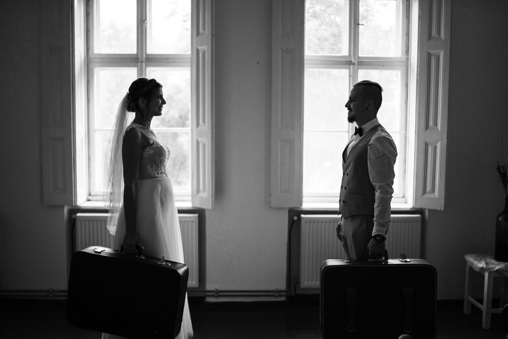 Two silhouetted figures stand facing each other in front of bright windows in a minimalist room.