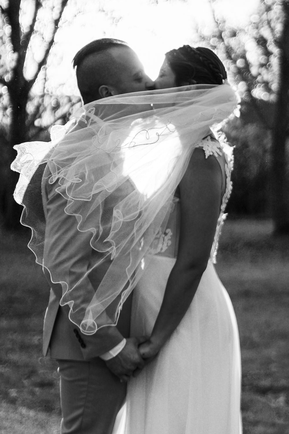 Black and white wedding portrait series showing couple embracing with bride's veil flowing in romantic outdoor setting.