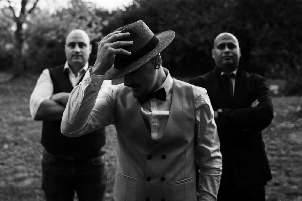 Three people in black and white photo with person in center wearing light suit and hat making expressive gesture.