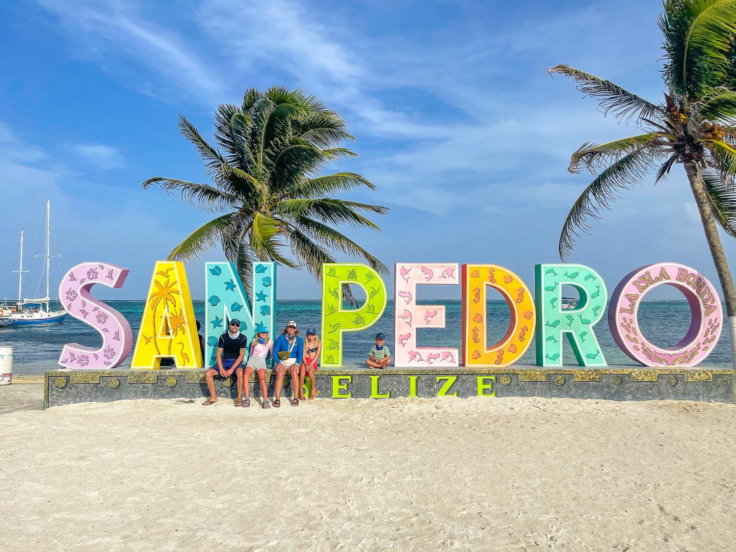 Colorful San Pedro sign with large letters sits on a tropical beach with palm trees and blue sky in Ambergris Caye, Belize.