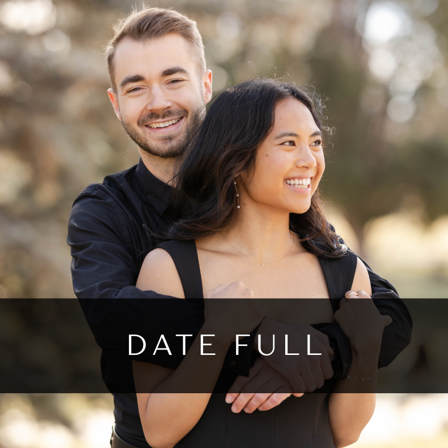 A joyful couple embraces outdoors in matching black attire during a romantic photoshoot session.
