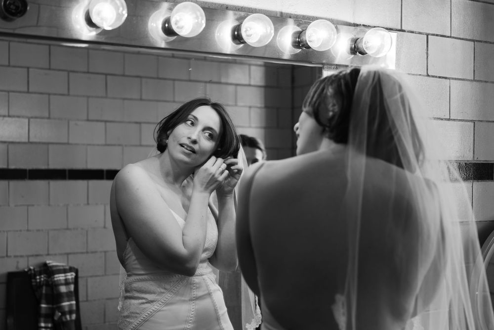 Black and white photo of performers preparing in a dressing room with vanity lights.