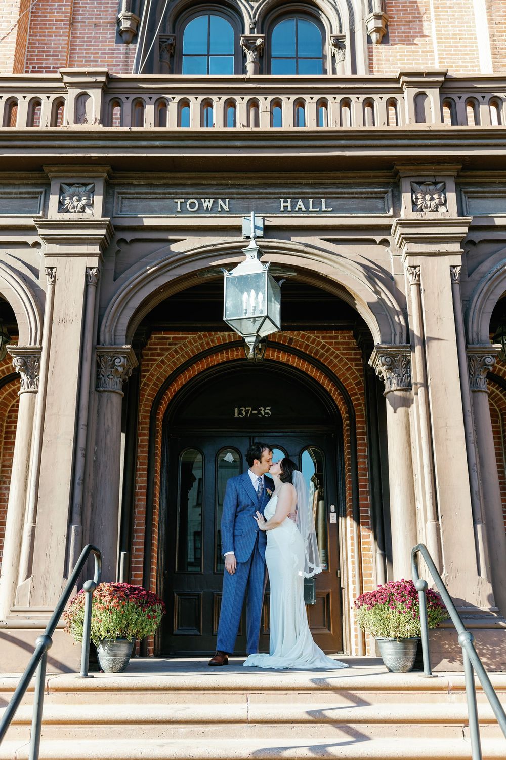 A couple poses for wedding photos in front of a historic Town Hall building with ornate stone architecture.