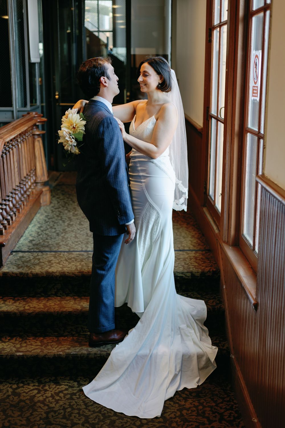 A couple shares an intimate moment on an ornate staircase in formal wedding attire.