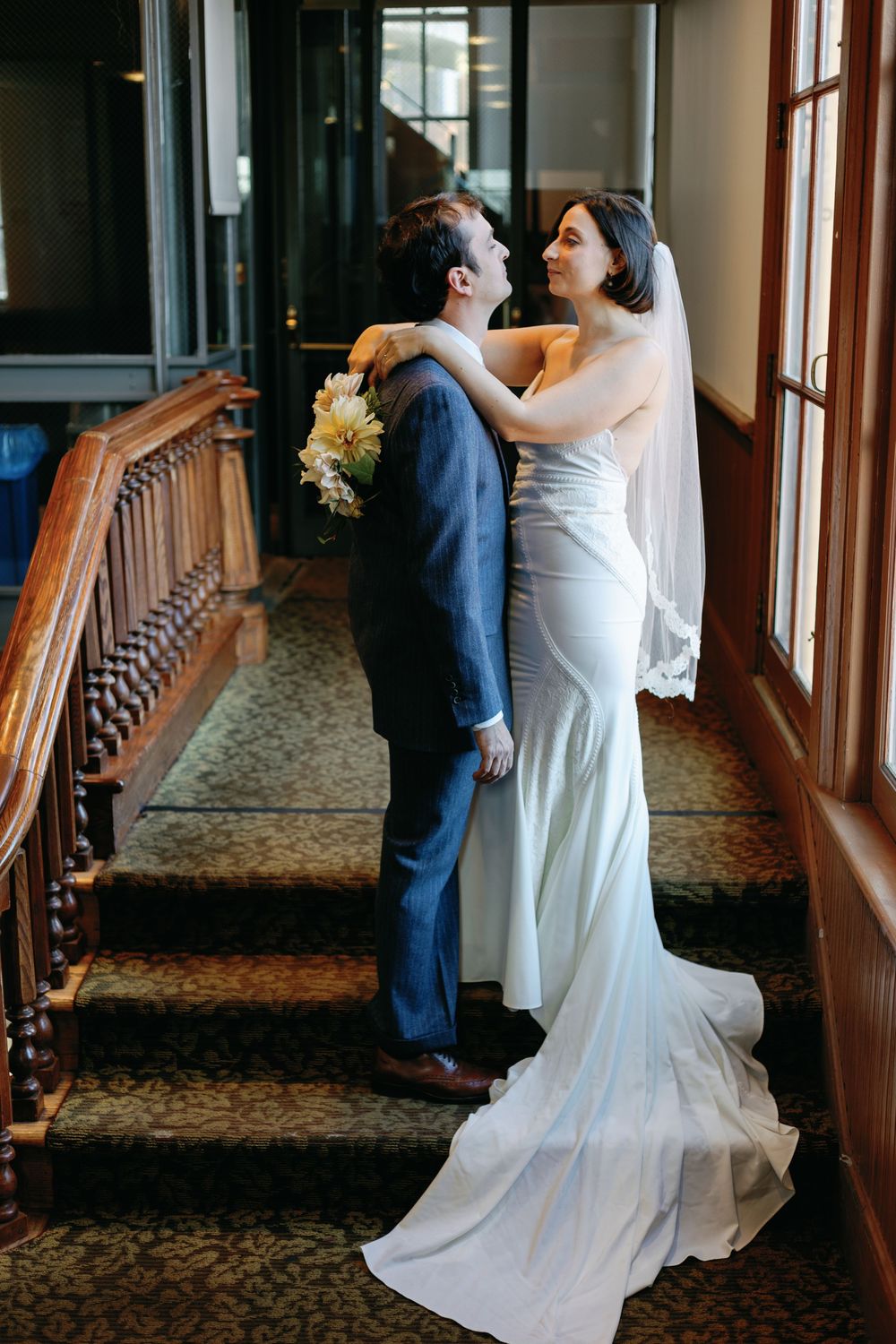 A wedding couple embracing on ornate wooden staircase.
