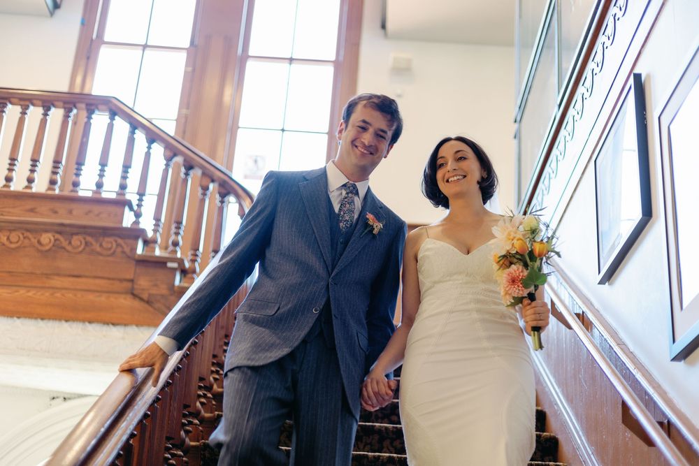 Couple walking down a wooden staircase in formal attire.