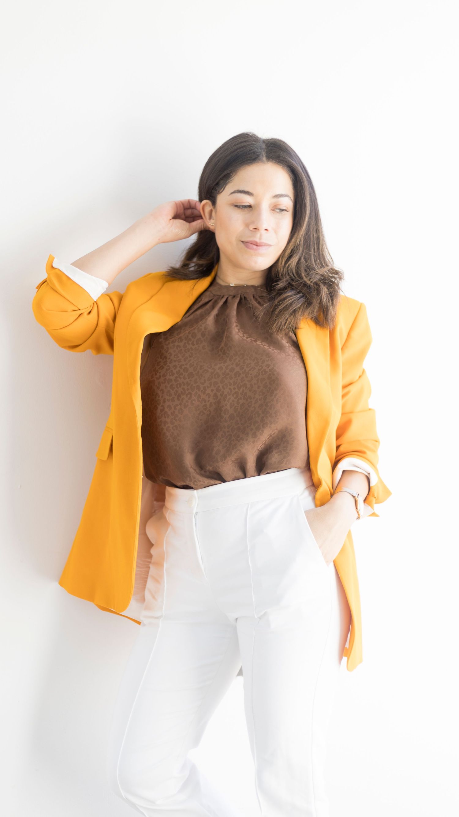 Stylish outfit featuring mustard blazer, brown top and white pants against white background.