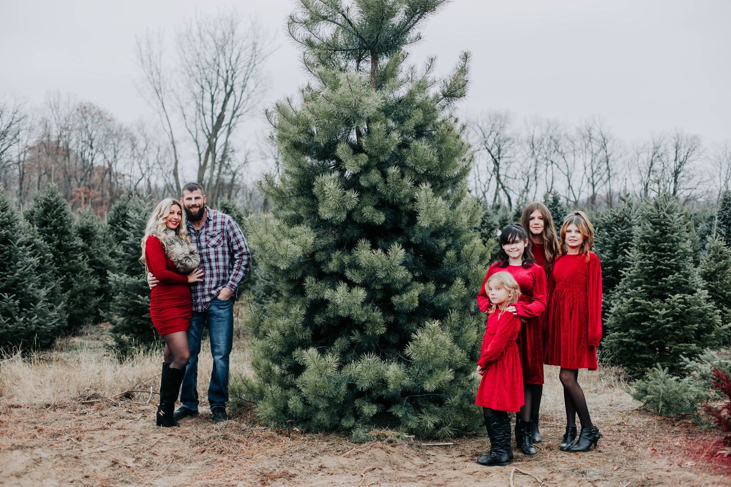 Winter family photoshoot among evergreen trees in matching red and plaid outfits.