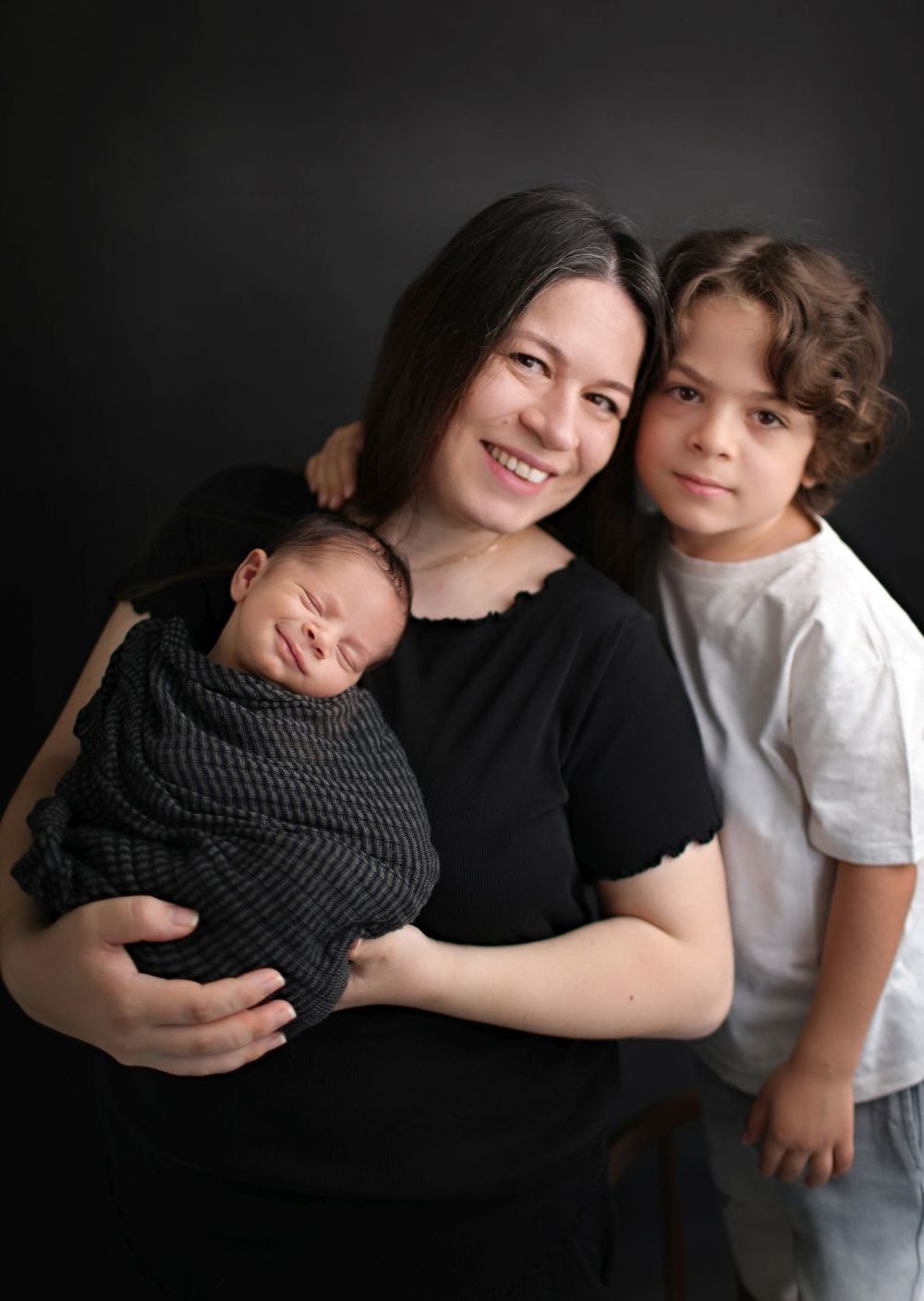 A family portrait featuring a mother with her children against a dark background.