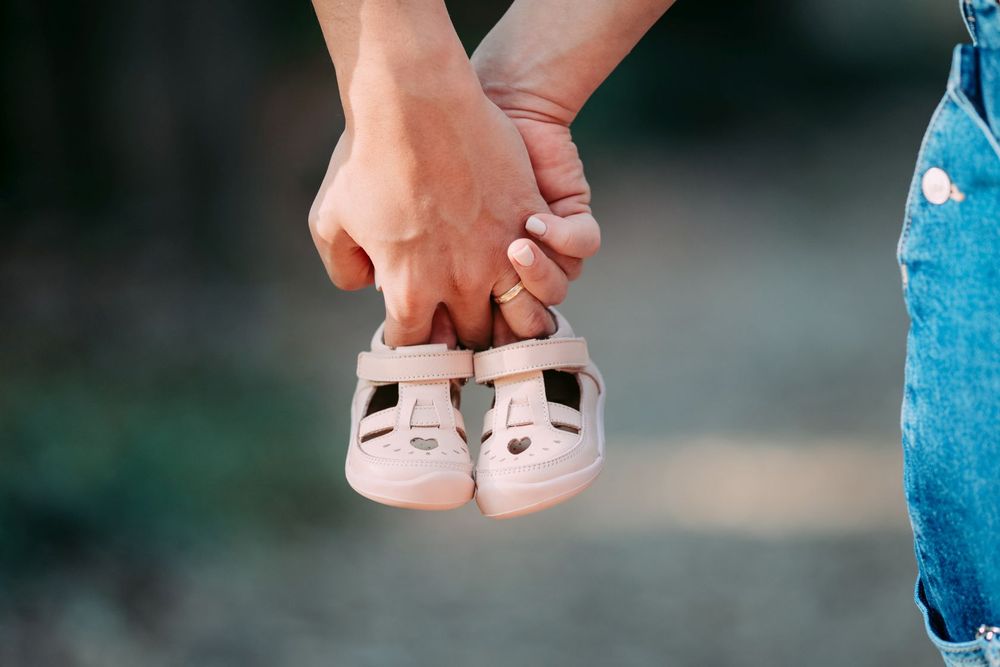 Close-up of hands holding small pink baby shoes against a blurred background.
