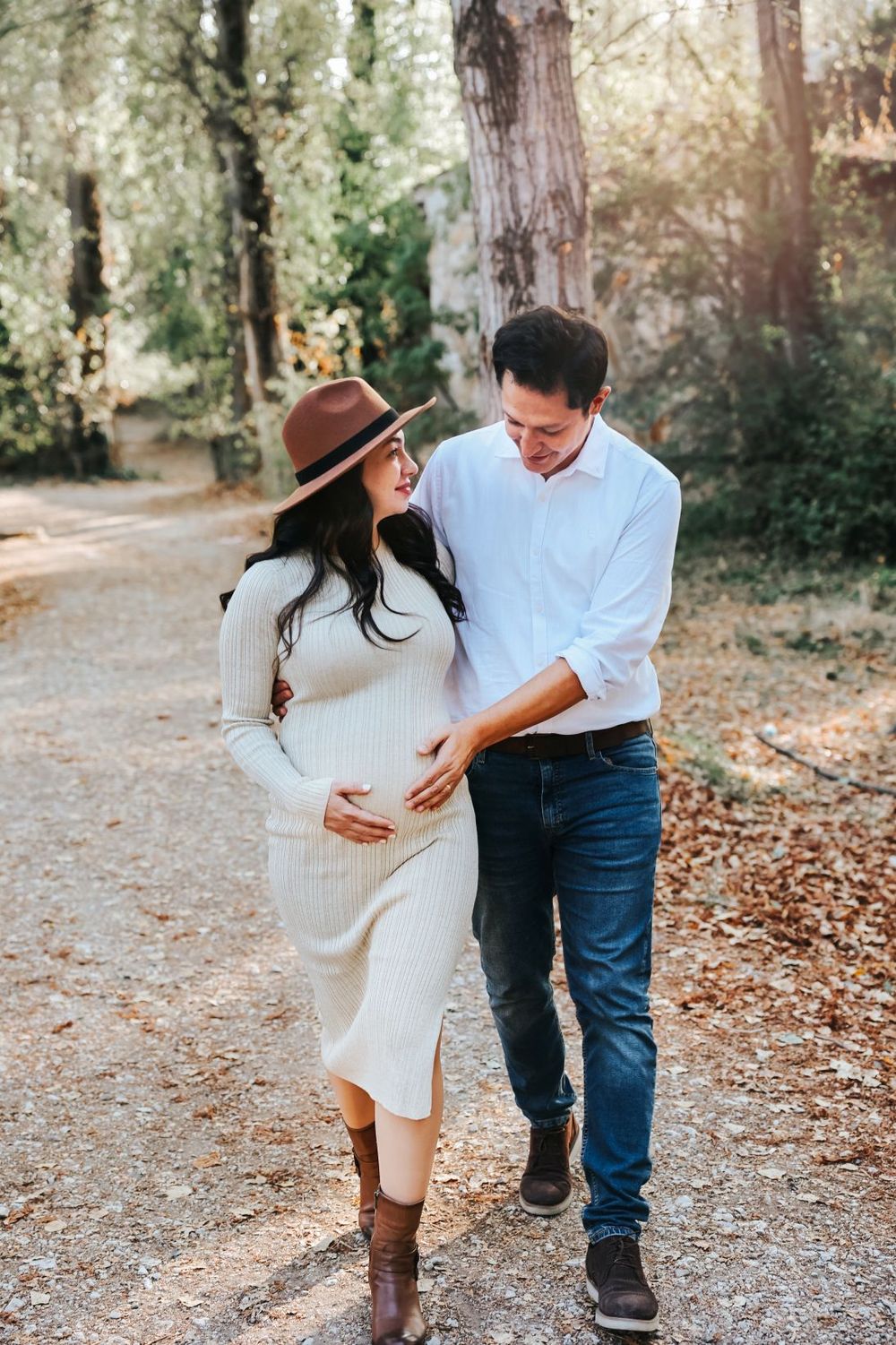 A couple takes a romantic walk on a forest path during an autumn maternity photoshoot.