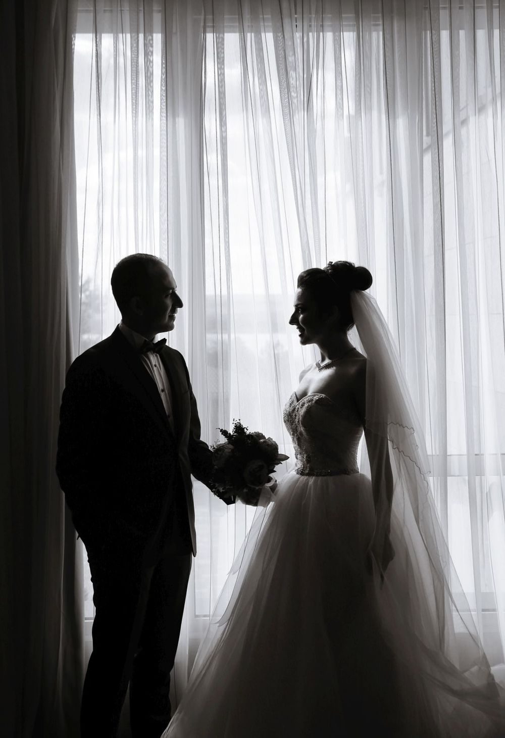 A silhouette of a bride and groom against sheer white curtains in dramatic lighting.