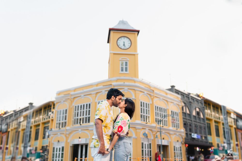 Romantic couple embracing in front of a yellow colonial building with a clock tower.