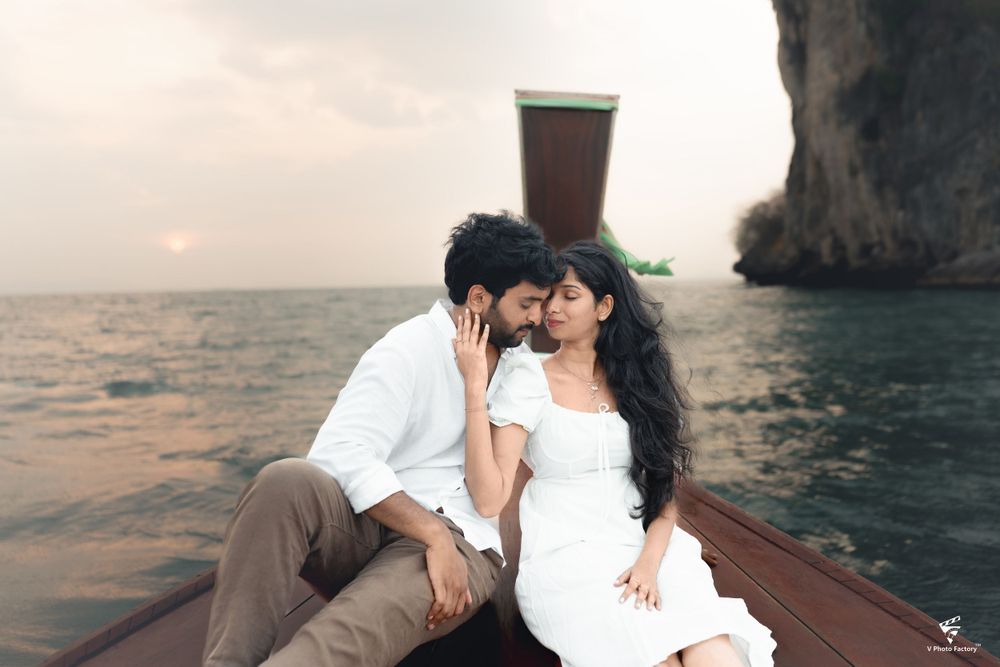 A romantic moment captured on a wooden boat at sea during sunset with dramatic cliffs in the background.