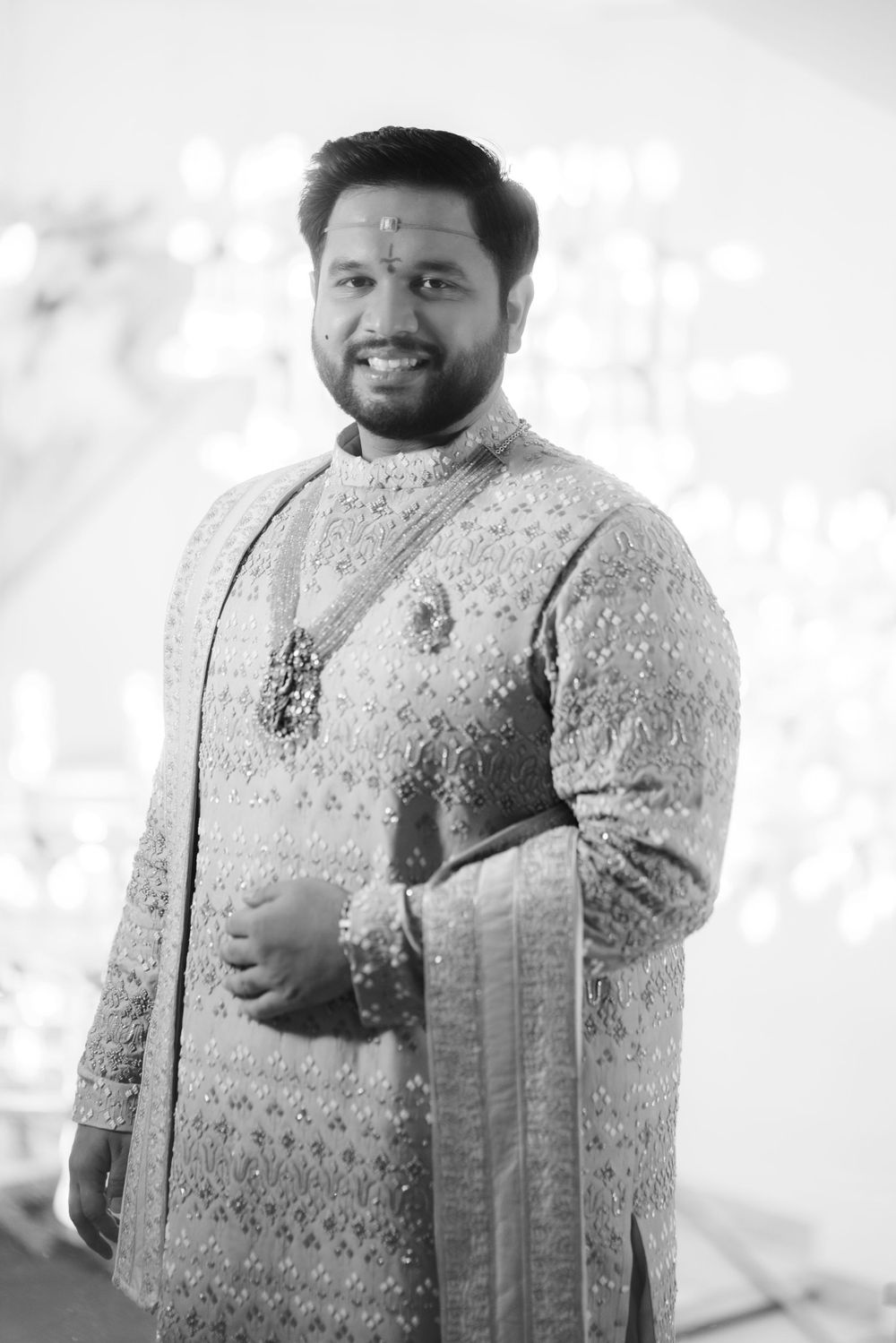 Black and white portrait of a groom in an embroidered traditional Indian sherwani.