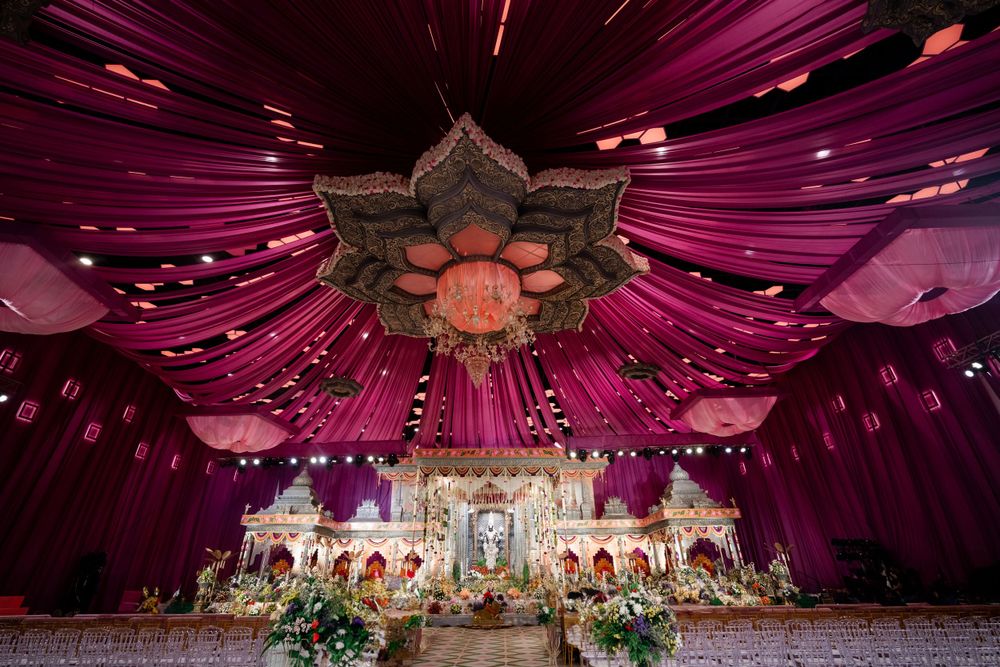 Elegant purple and pink wedding mandap decoration with dramatic ceiling draping and lighting.