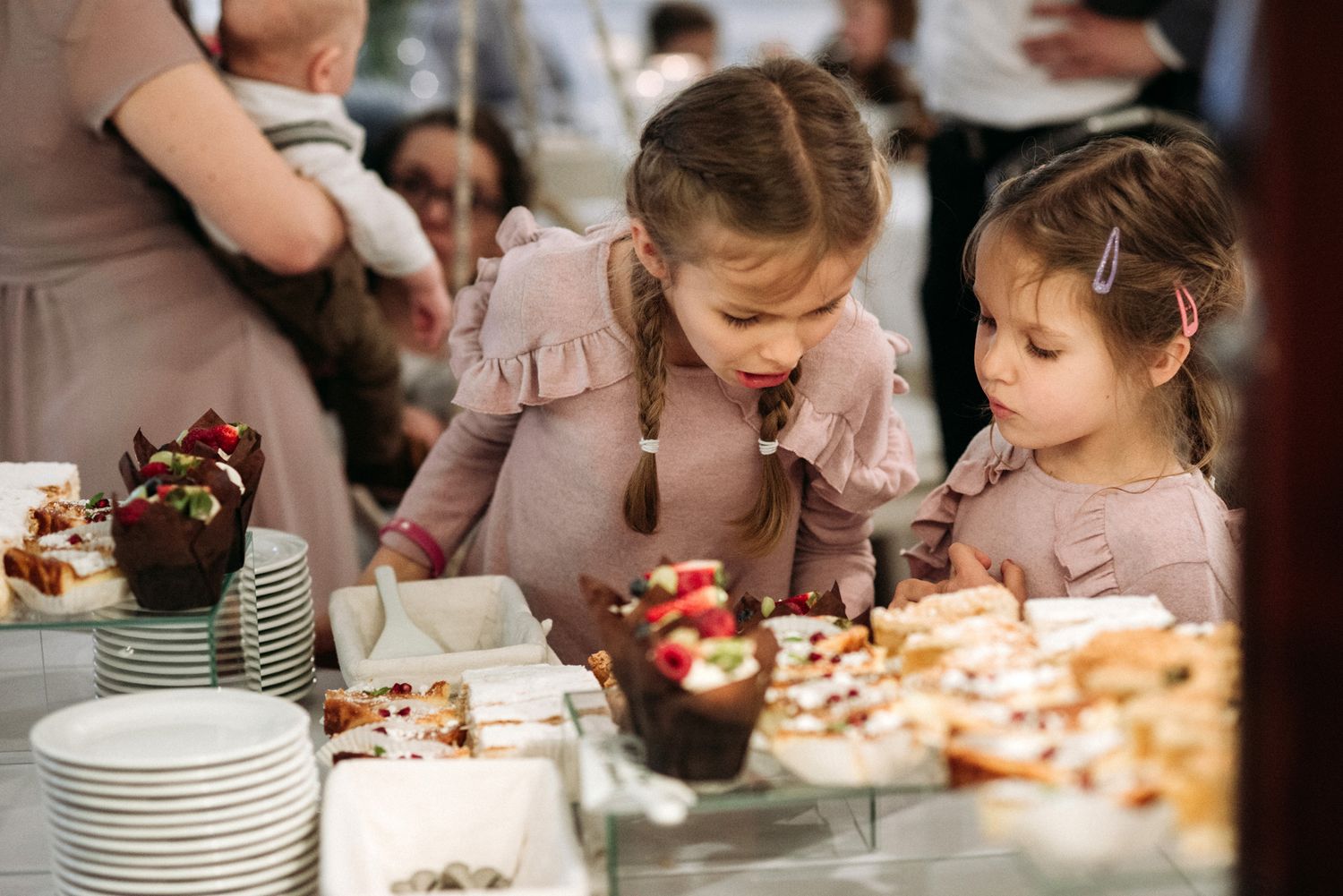 People gather around a decorated dessert table with cakes and white plates at a celebration event.