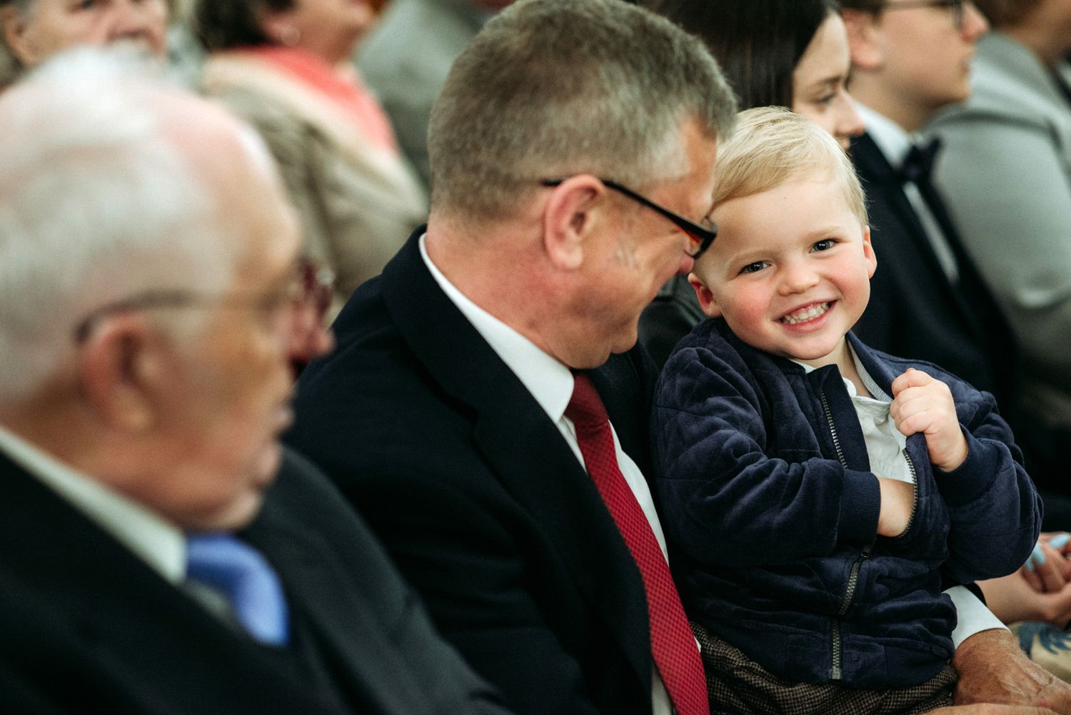 A child laughs joyfully while sitting with adults in formal attire at an event.