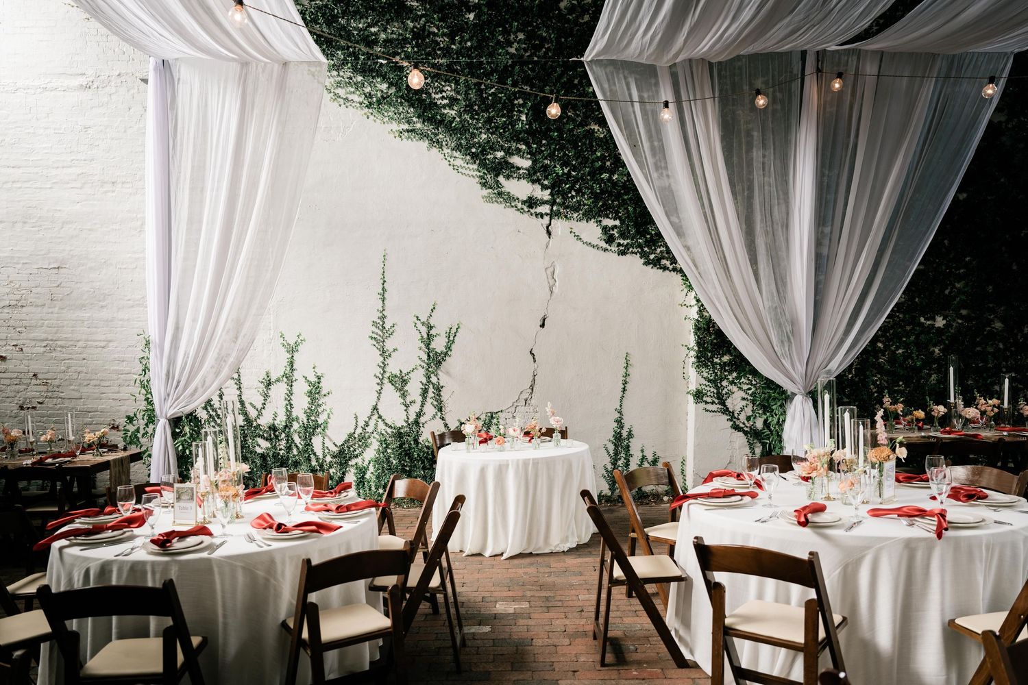 White draped fabric and elegant table settings create a romantic outdoor wedding reception atmosphere.