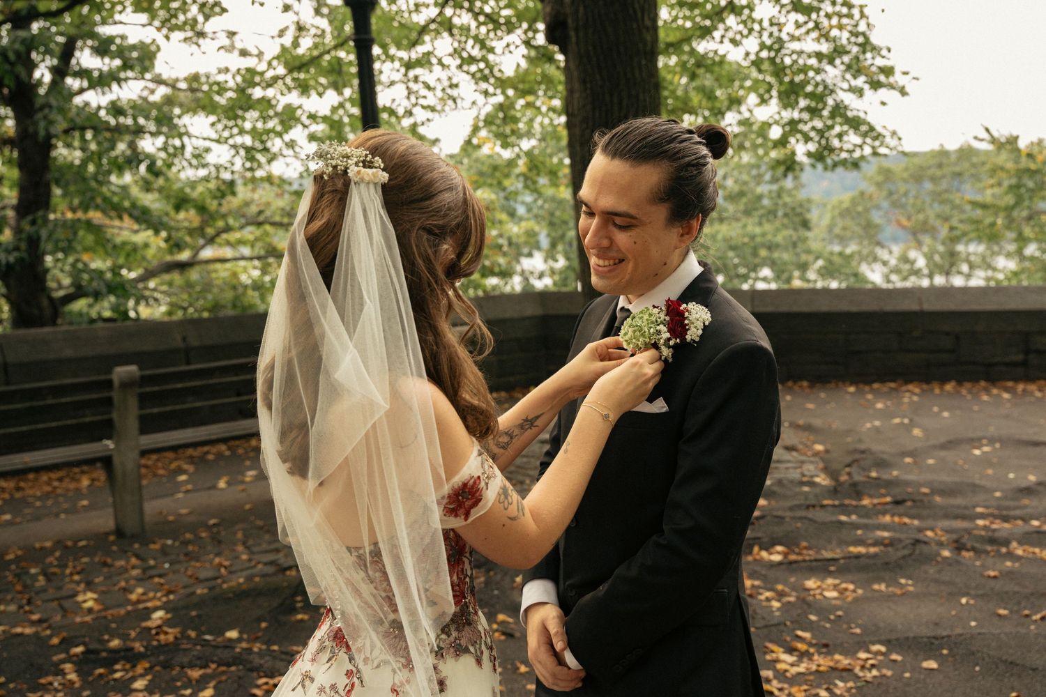 Bride adjusting groom's boutonniere outdoors during fall wedding ceremony.