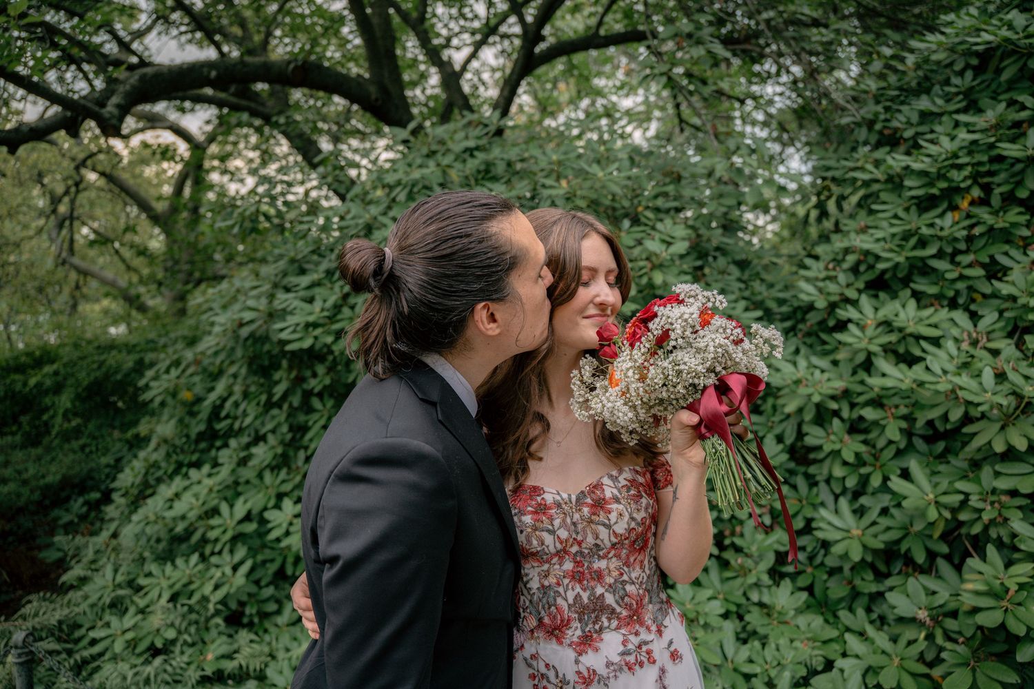 Groom kissing bride's cheek as she holds a red and white wedding bouquet.