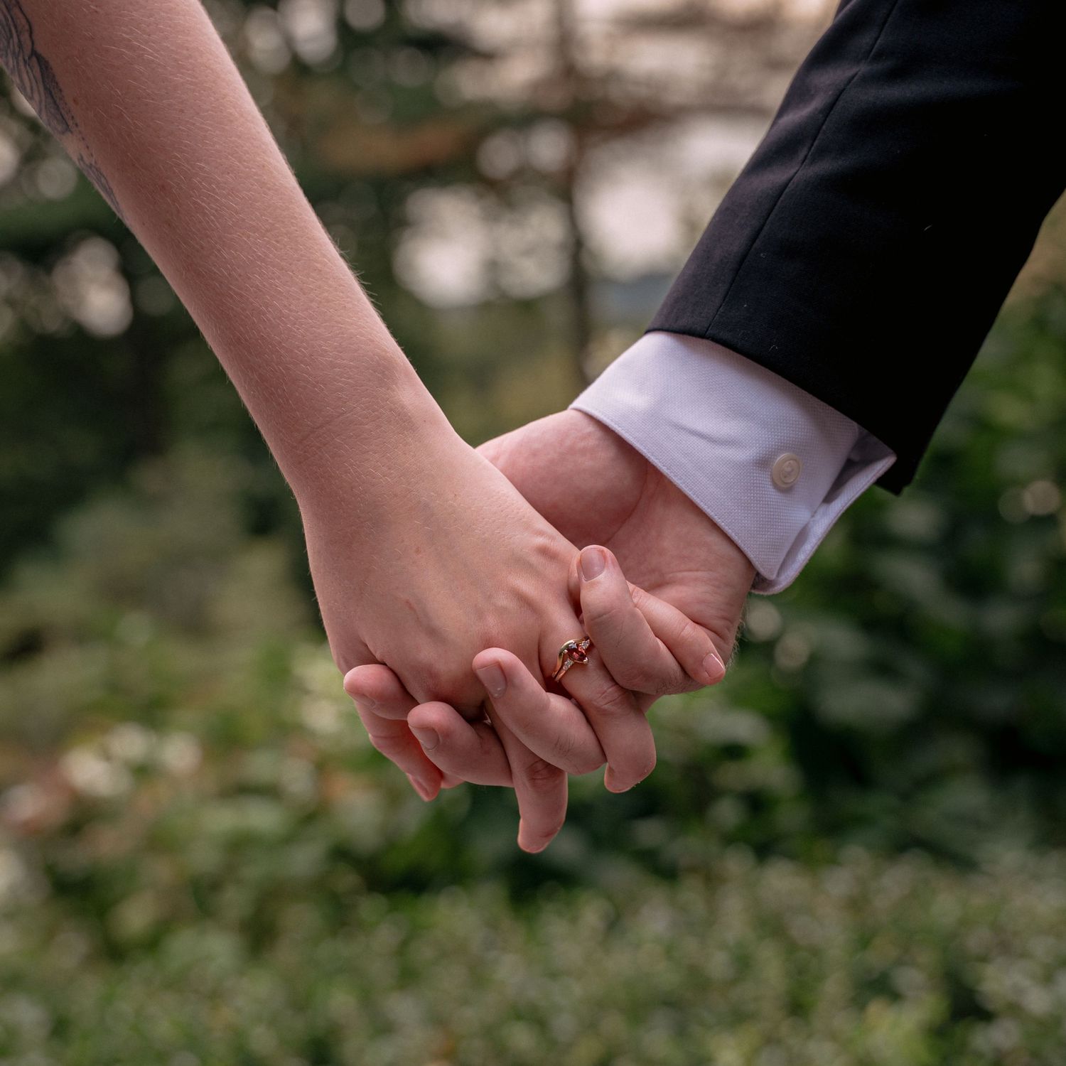 Close-up of bride and groom holding hands with wedding ring visible.