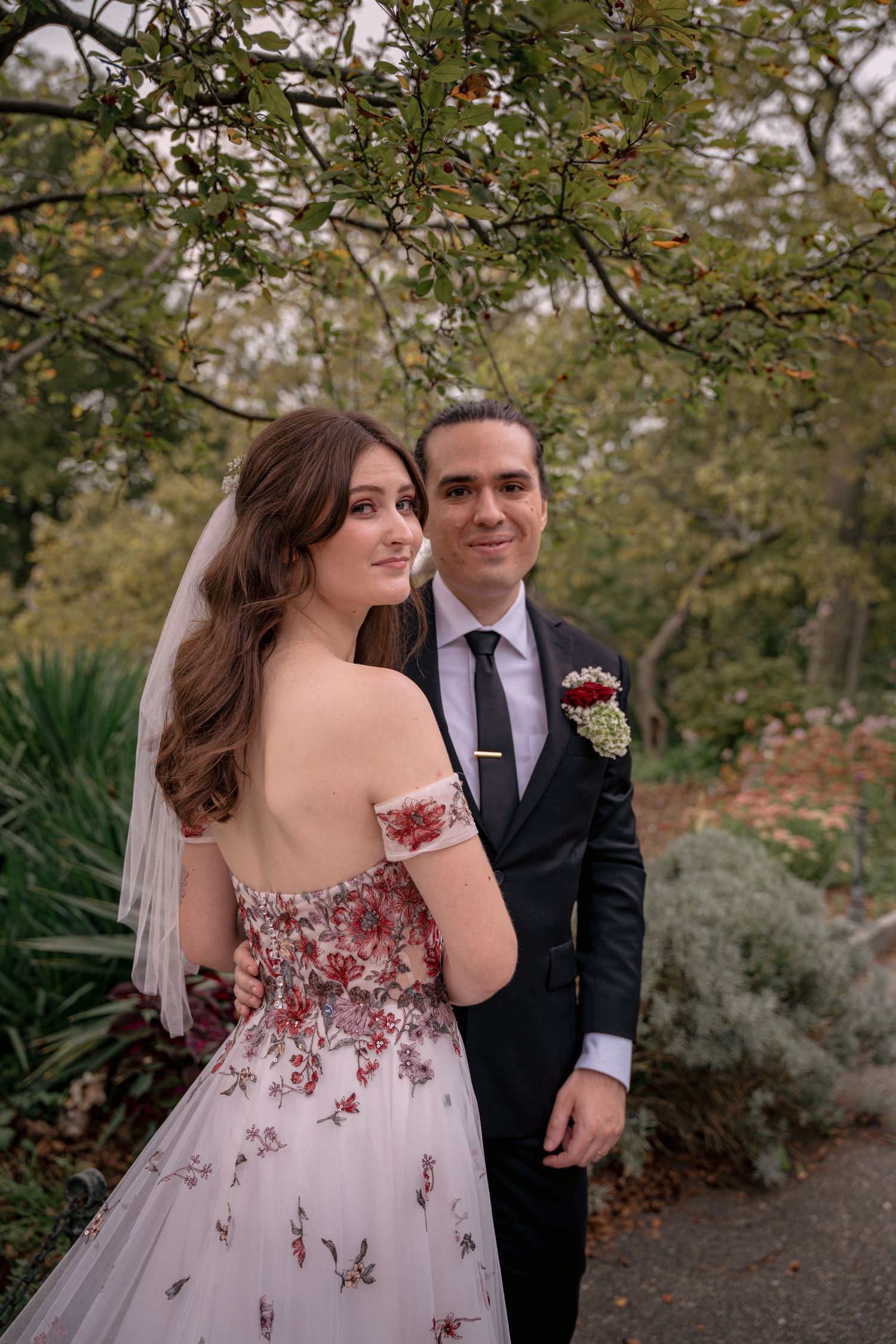 Bride in floral off-shoulder gown and groom posing in autumn garden.