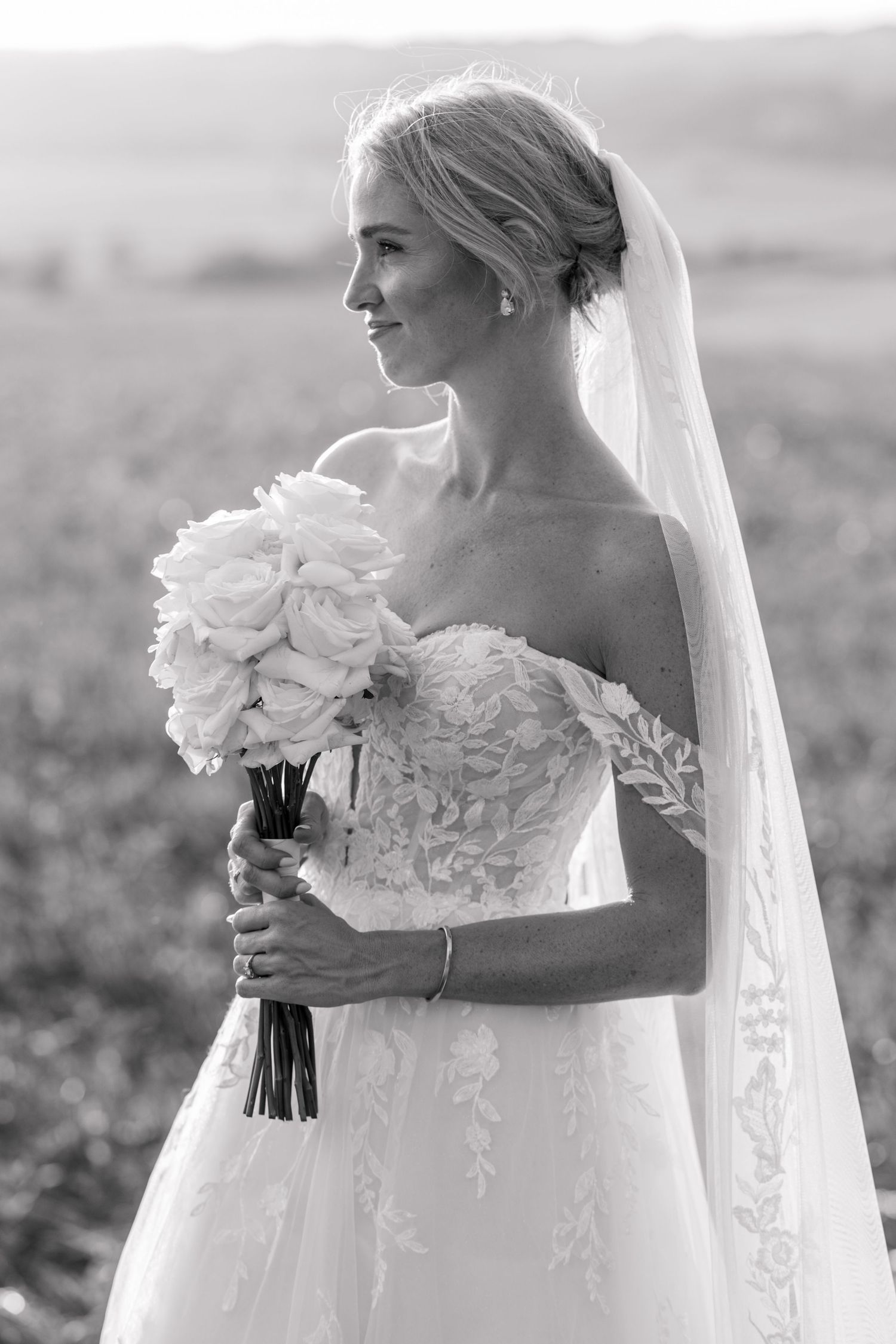 A bride in an elegant off-shoulder wedding gown with floral details holds a white bouquet in a black and white photo series.