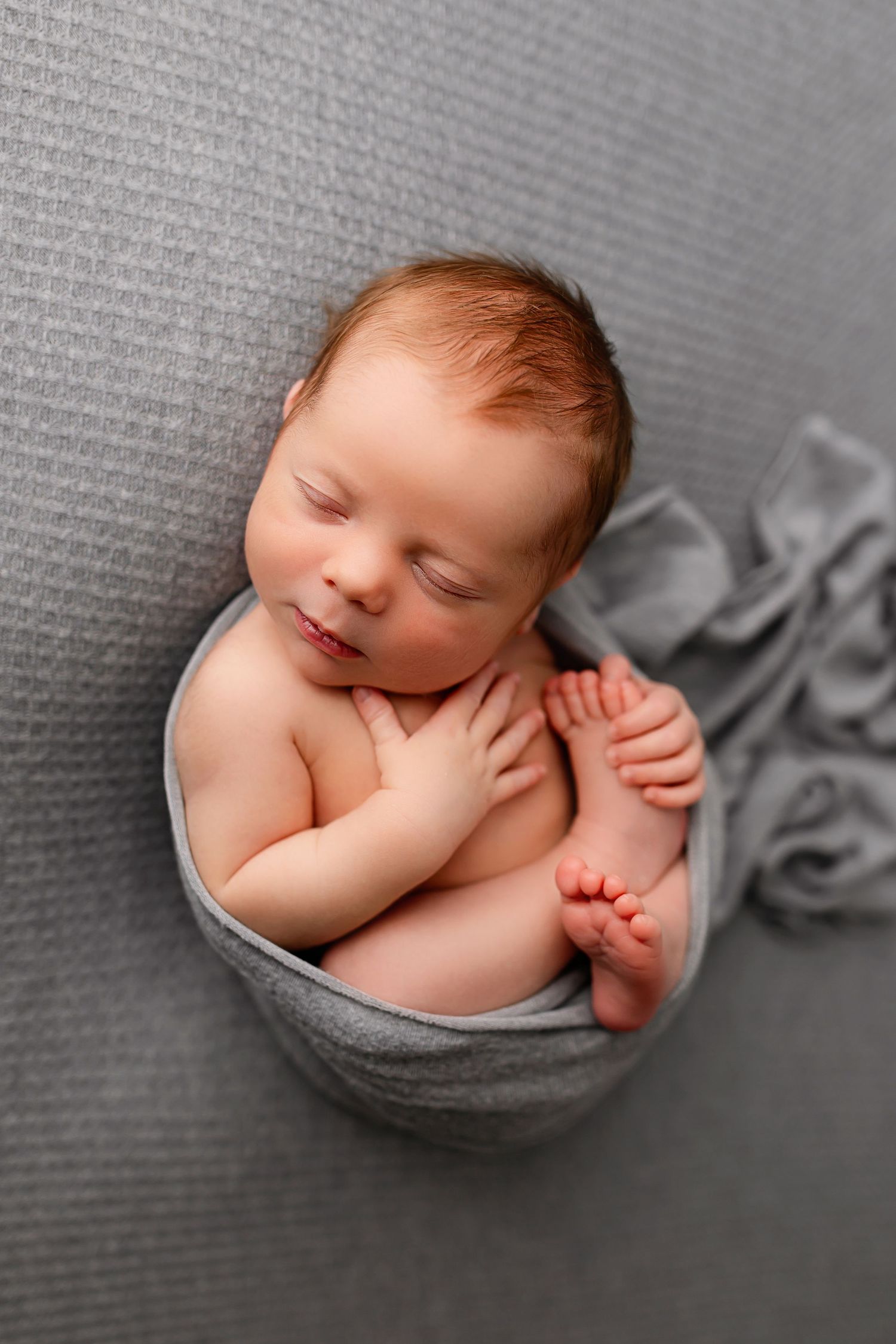 Sleeping newborn baby boy curled up in gray wrap on gray backdrop at Flowertown Photography studio