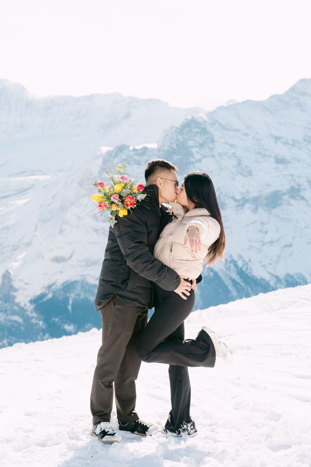 A romantic winter moment shared between a couple in the snowy mountains with a colorful bouquet of flowers.