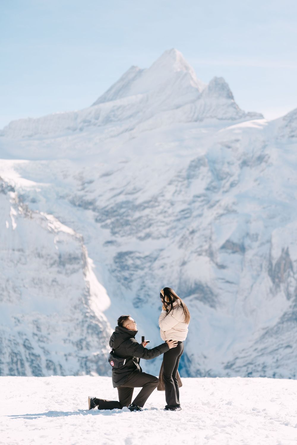 A marriage proposal scene against snowy mountain peaks with a dramatic glacier backdrop in winter.