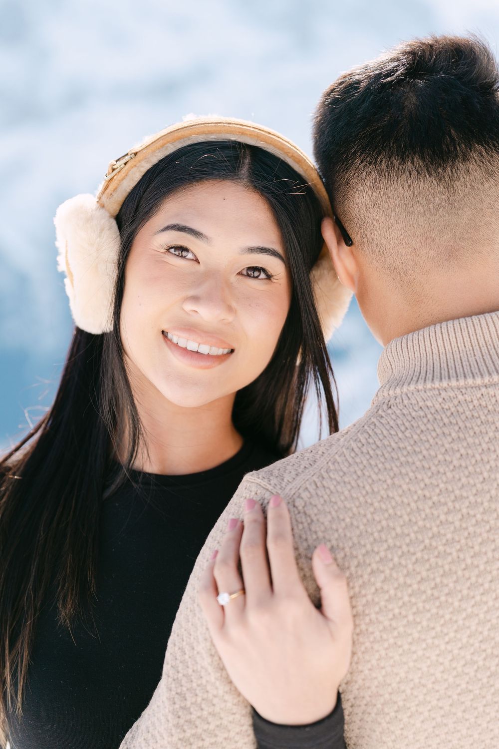 A couple shares an intimate winter moment outdoors as one person wears cozy earmuffs and a black sweater.
