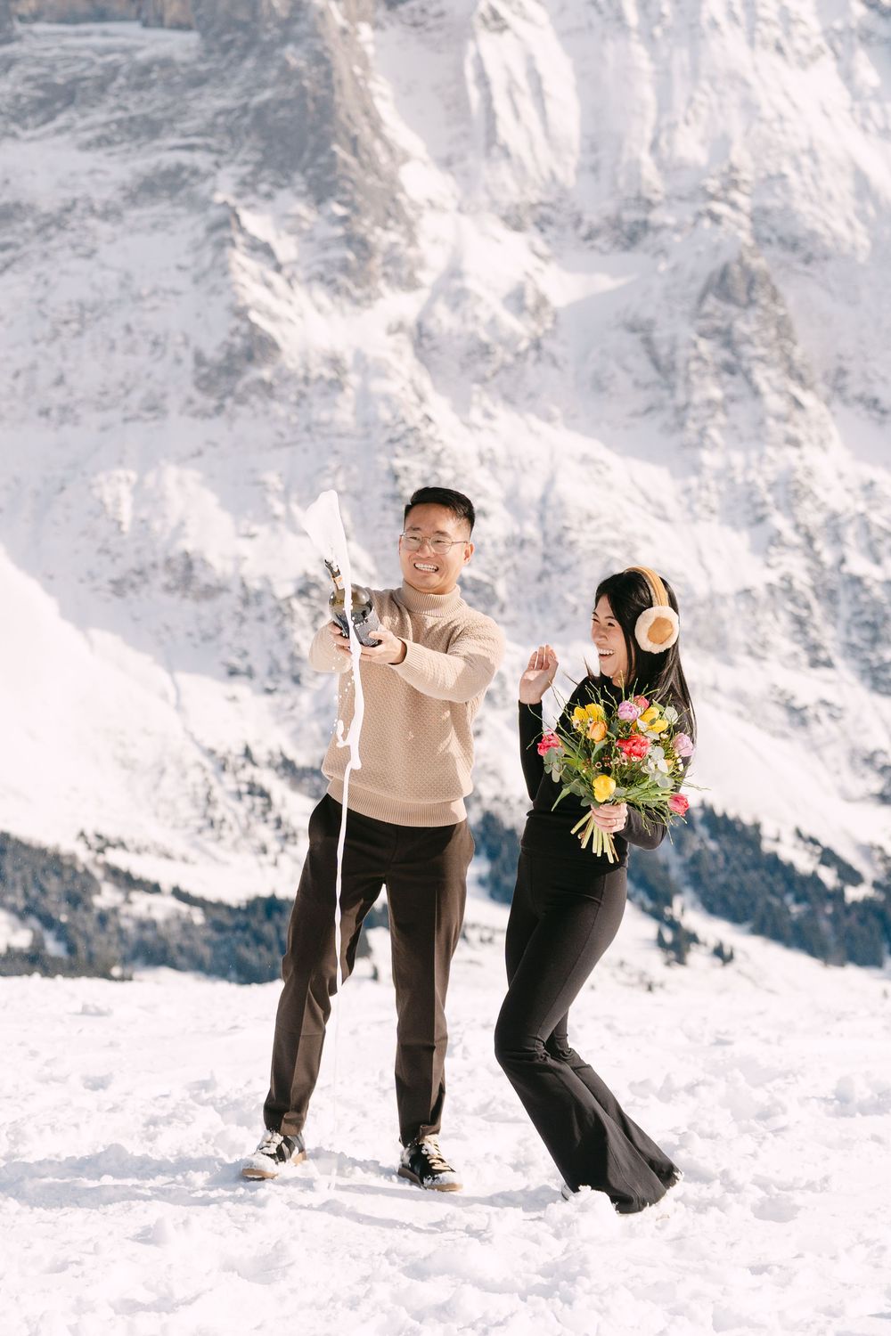 A couple enjoying a winter day in the snowy Dolomites mountains, with one holding a colorful bouquet of flowers.