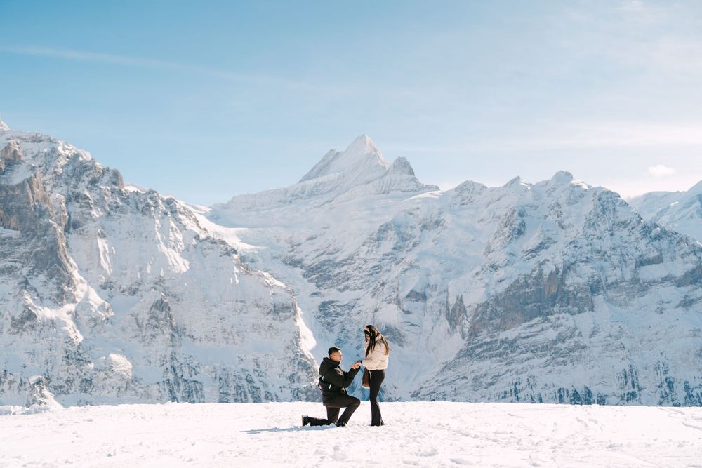 Two people snowboarding down a snowy mountain slope with majestic snow-capped peaks in the background.