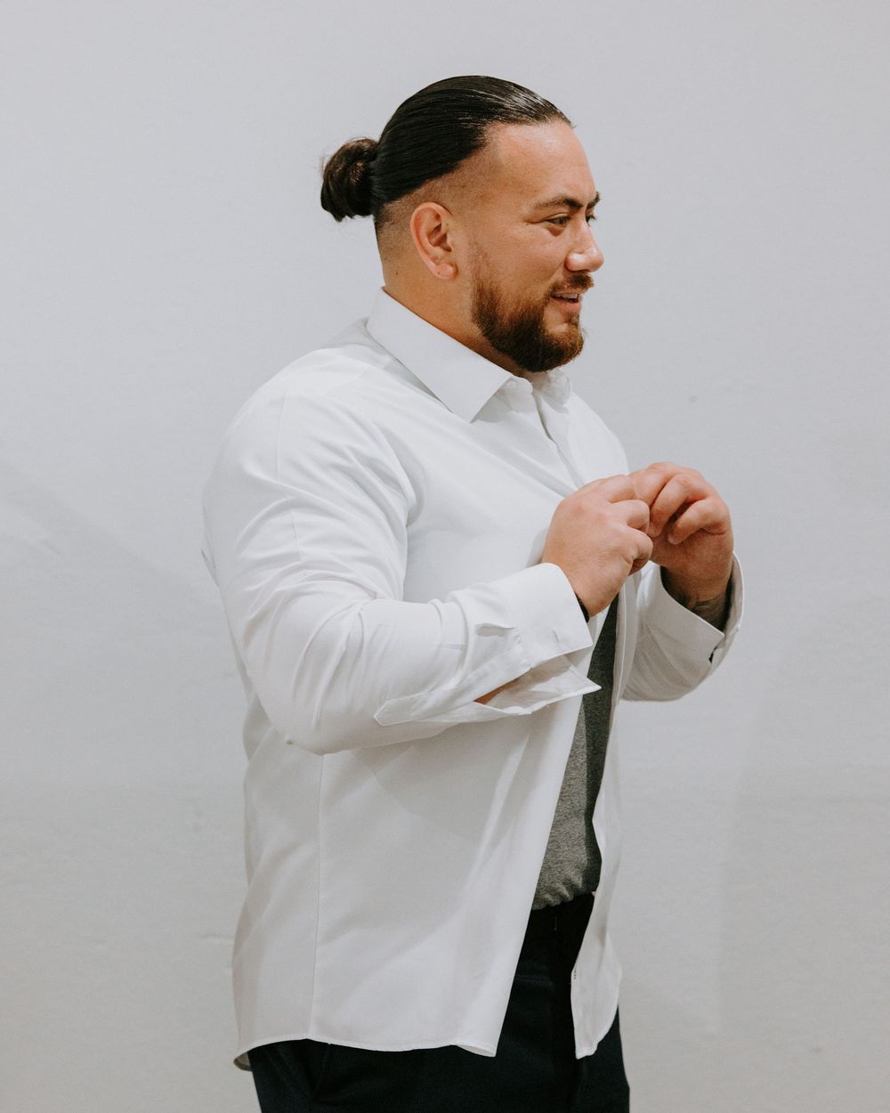Groom in white dress shirt fastening buttons while getting ready for wedding ceremony.