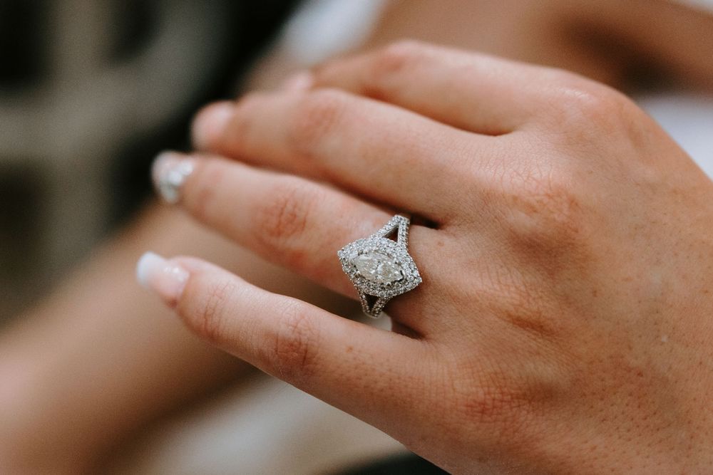 Close-up of elegant diamond halo engagement ring on bride's hand with manicured nails.